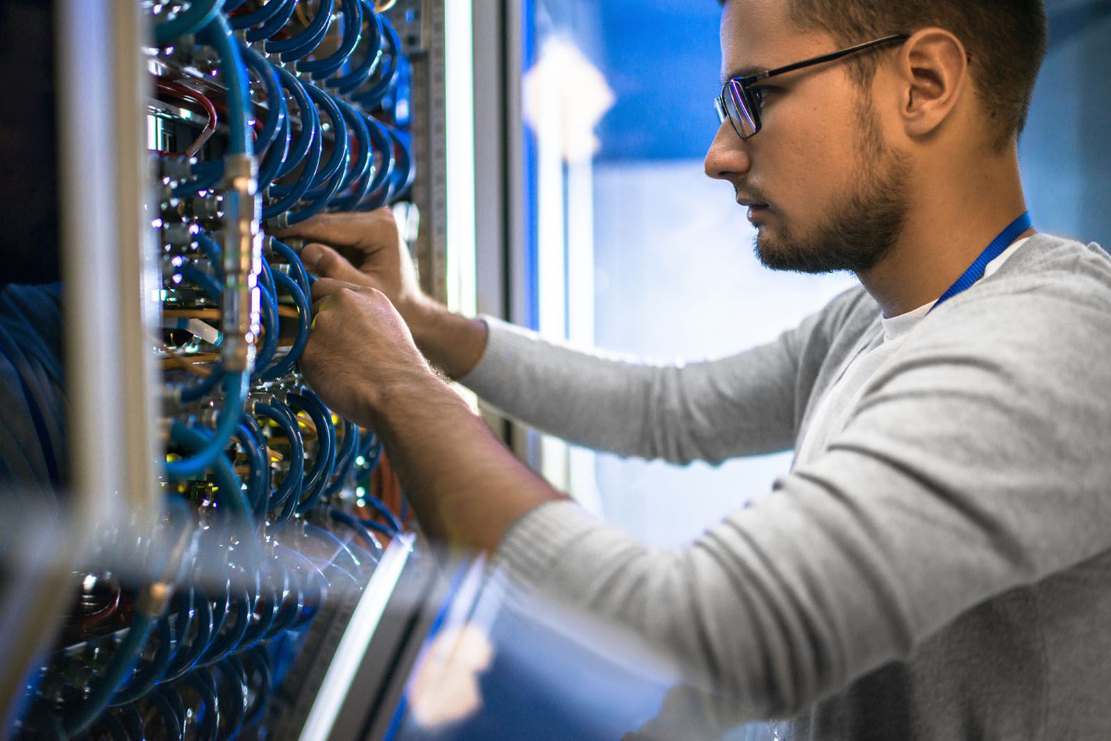 Picture of a male technician with glasses working on wiring a server with blue cables.